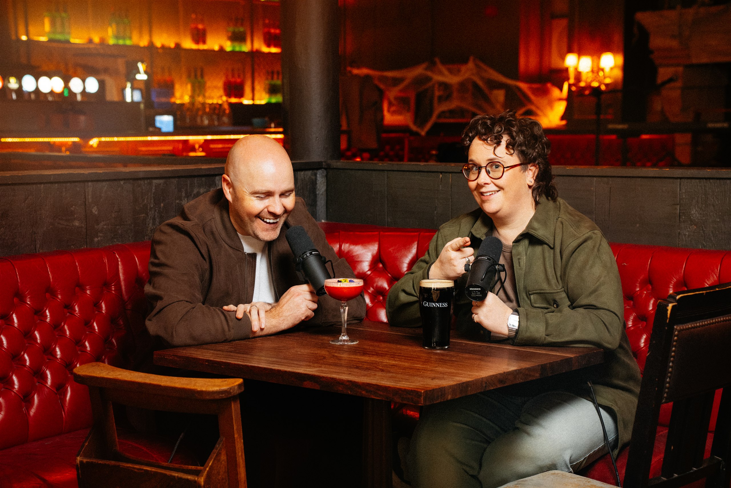 Paddy and Emer sharing a laugh with microphones in a warmly lit pub